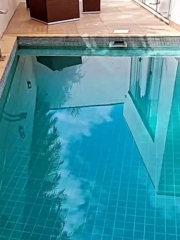 Depois: a mesma piscina com água cristalina, azulejos azuis visíveis e o céu refletido