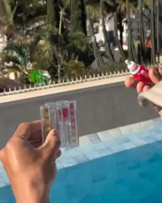 Mão segurando o kit de teste de cloro e pH ao lado da piscina