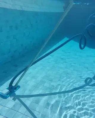 Aspirador de piscina passando no fundo de azulejos, visto embaixo d'água