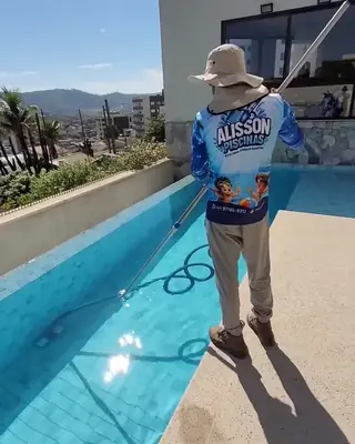 Alisson de costas com o uniforme da empresa, limpando uma piscina de borda infinita